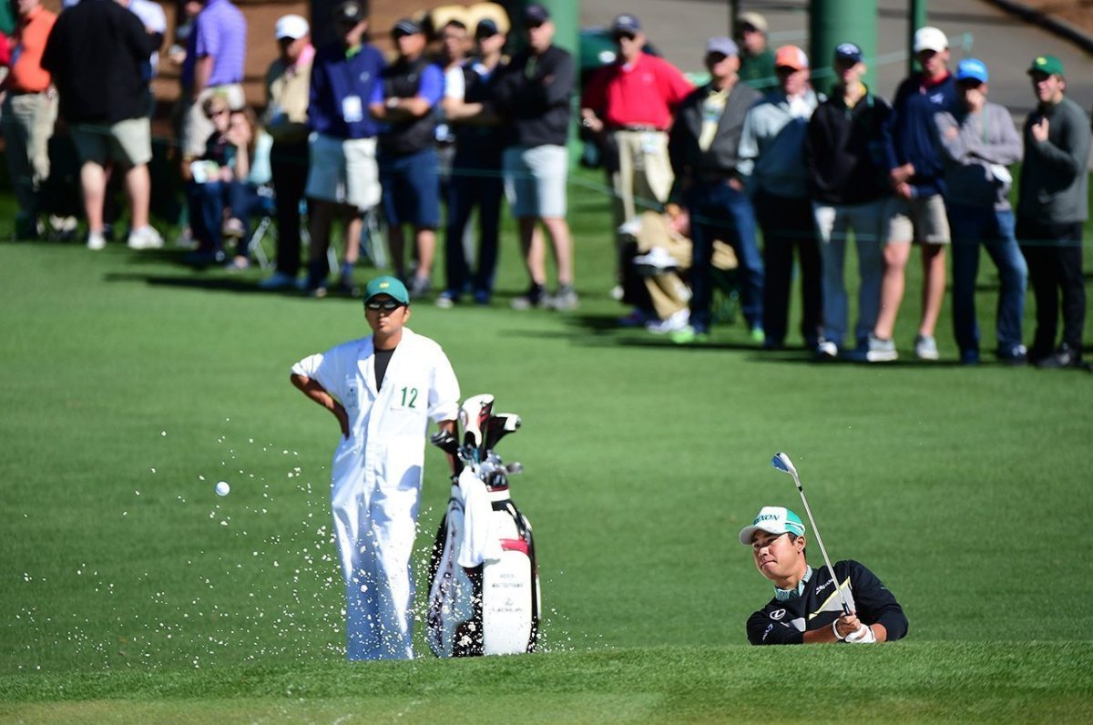 Hideki Matsuyama of Japan plays a shot from a bunker on the second hole as caddie Daisuke Shindo looks on during the first round of the 2016 Masters Tournament at Augusta National Golf Club.